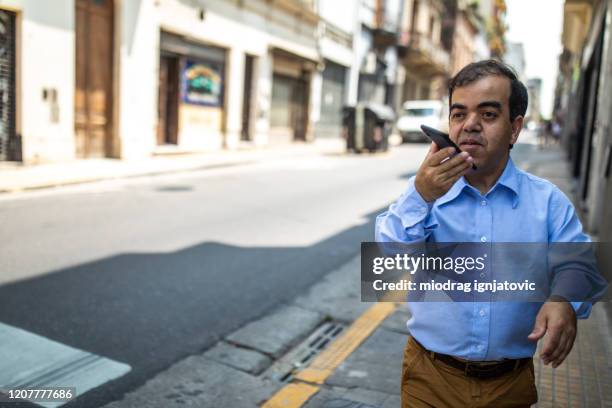 businessman with dwarfism sending voice message using smart phone while walking on a sidewalk - ana imagens e fotografias de stock