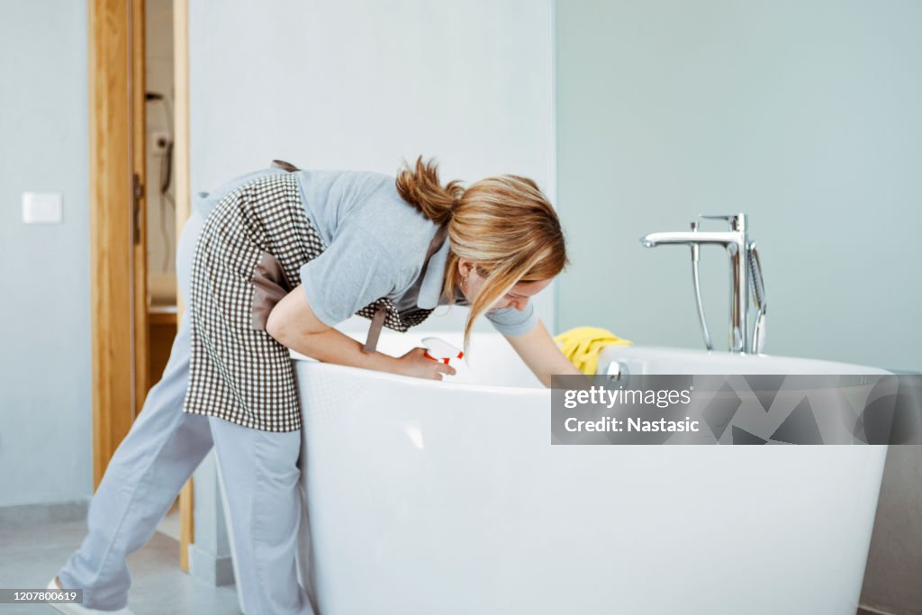 Mujer joven haciendo tareas domésticas, limpiando la bañera del baño