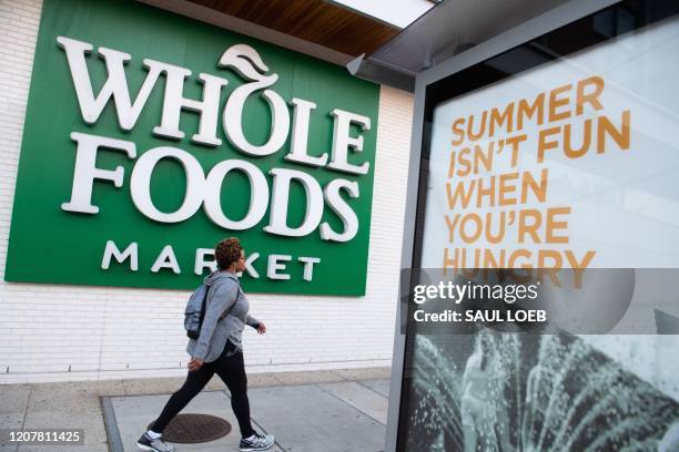 Woman walks past a Whole Foods supermarket in Washington, DC, March 20, 2020. - Whole Foods, like several other retailers, is reserving some hours...