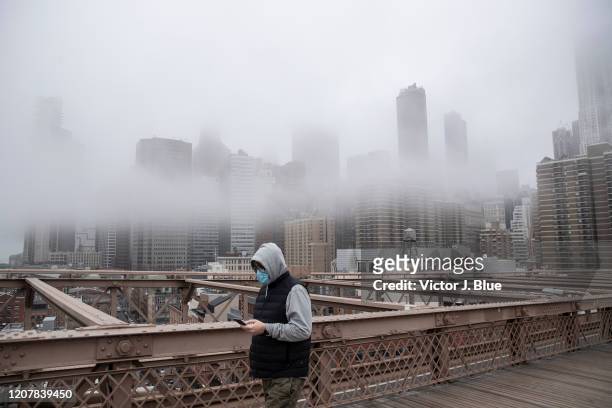 Man wearing a mask walks the Brooklyn Bridge in the midst of the coronavirus outbreak on March 20, 2020 in New York City. The economic situation in...