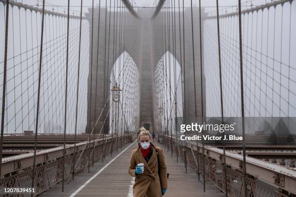 Woman wearing a mask walks the Brooklyn Bridge in the midst of the coronavirus outbreak on March 20, 2020 in New York City. The economic situation in...