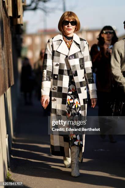Anna Wintour wears sunglasses, a bejeweled necklace, a black and white checkered long trench coat, a floral print dress, boots, outside Marni, during...