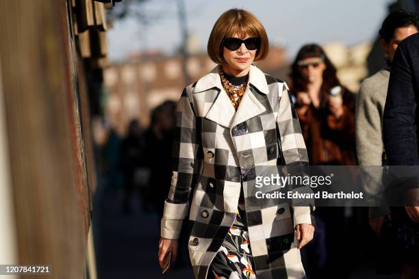 Anna Wintour wears sunglasses, a bejeweled necklace, a black and white checkered long trench coat, a floral print dress, outside Marni, during Milan...