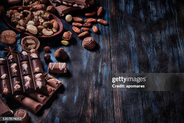 low-key-bild einer vielzahl von schokolade und bombonen mit getrockneten früchten. altmodischer stil auf einem blauen rustikalen tisch mit kopierraum - bombones chocolate stock-fotos und bilder