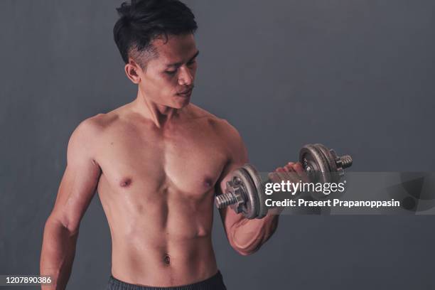 athletic shirtless young male fitness model holding dumbbell for workout bodybuilding and muscles - male stomach stock-fotos und bilder