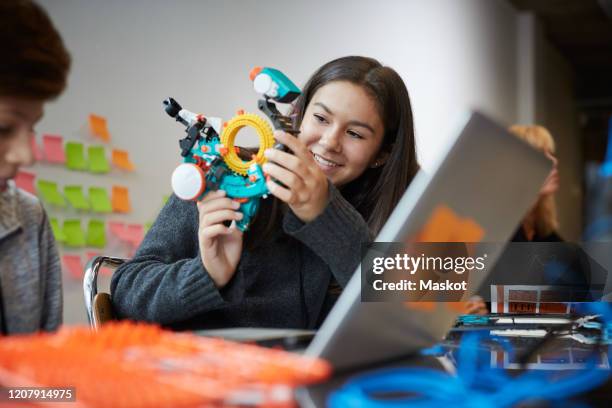 smiling girl experimenting with model while sitting by male in science classroom - ricerca di scienze foto e immagini stock