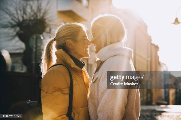 happy woman embracing female partner with closed eyes while standing in city - couple winter stock pictures, royalty-free photos & images