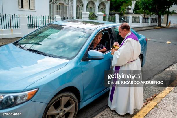 Monsignor Jose Emilio Cummins gives the eucharist, communion, to Iris Sepulveda as she sits in her car in front of the Nuestra Senora del Perpetuo...