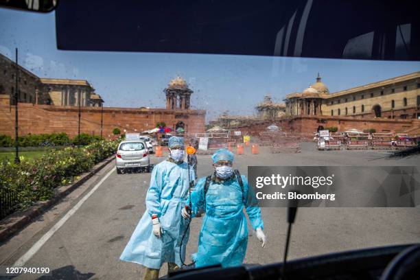 Security personnel wearing protective suits and masks spray disinfectant towards the windshield of a bus outside the South Block of the Central...