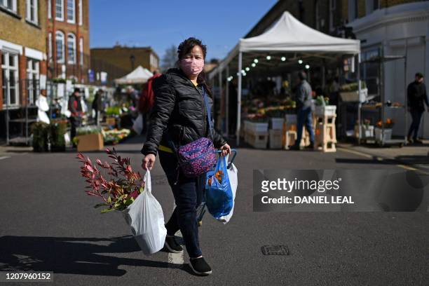 Woman wearing a protective face mask carries flowers after a visit to Columbia Road flower market in east London on Mother's Day, March 22, 2020. -...