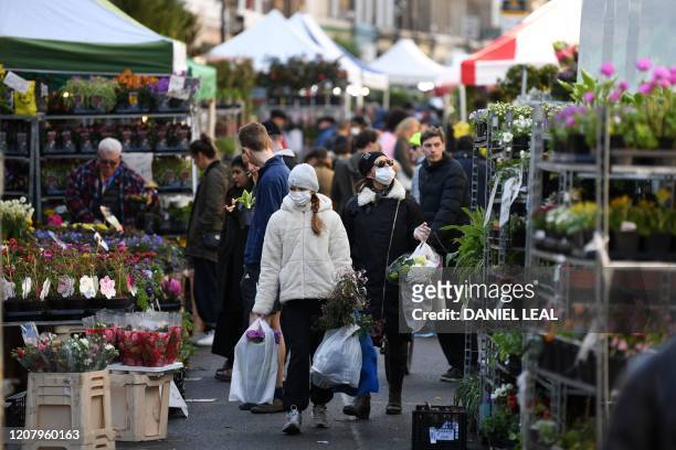 Shoppers wearing a protective face masks carry flowers after a visit to Columbia Road flower market in east London on Mother's Day, March 22, 2020. -...