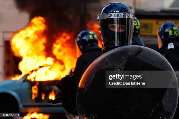 Riot police stand in front of a burning car during riots in Clarence Road, Hackney on August 8, 2011 in London, England. Pockets of rioting and...