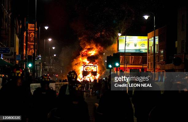 Double decker bus burns as riot police try to contain a large group of people on a main road in Tottenham, north London on August 6, 2011. Two police...