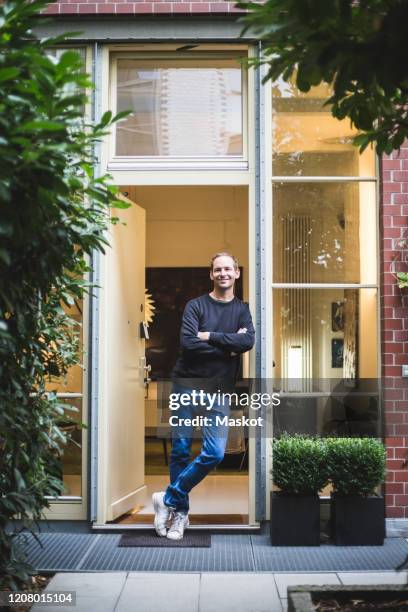 portrait of male architect standing with arms crossed at house entrance - apartment front door foto e immagini stock