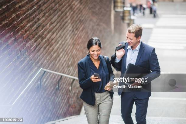 happy male and female entrepreneurs using phone while climbing staircase in city - stairs business stockfoto's en -beelden