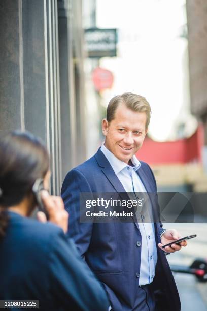 smiling mature businessman with smart phone looking at coworker outdoors - business meeting outside stock pictures, royalty-free photos & images