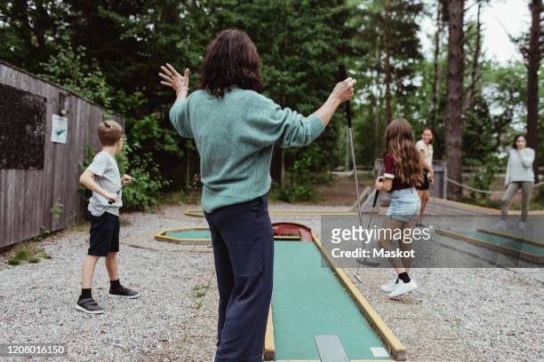 rear view of woman playing miniature golf with family in backyard - minigolf stockfoto's en -beelden