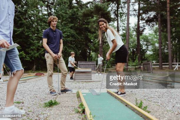 full length of smiling friends playing miniature golf in backyard during vacation - minigolf stockfoto's en -beelden