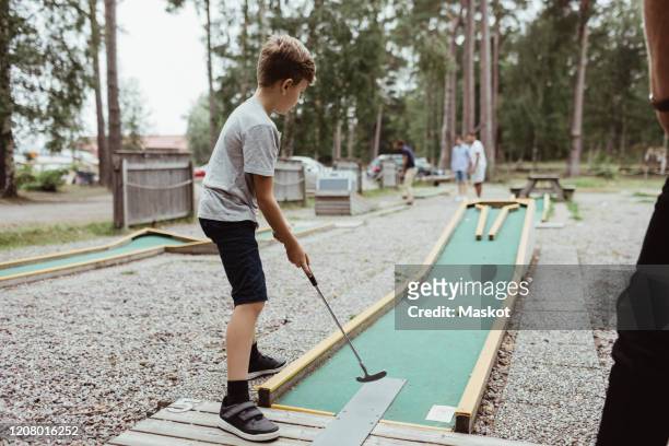 full length of boy playing miniature golf in backyard against tree - minigolf foto e immagini stock