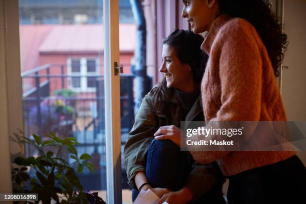 smiling lesbian couple looking through window at apartment during vacation - house rental stock pictures, royalty-free photos & images