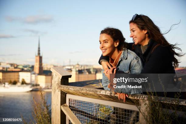 smiling lesbian couple standing at observation point in city against sky - stockholm city stock pictures, royalty-free photos & images