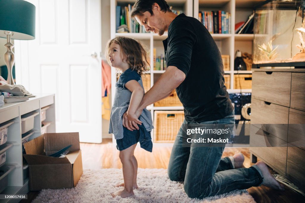 Father dressing daughter in living room