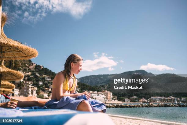 smiling girl sitting at beach against sky during sunny day - islas baleares fotografías e imágenes de stock