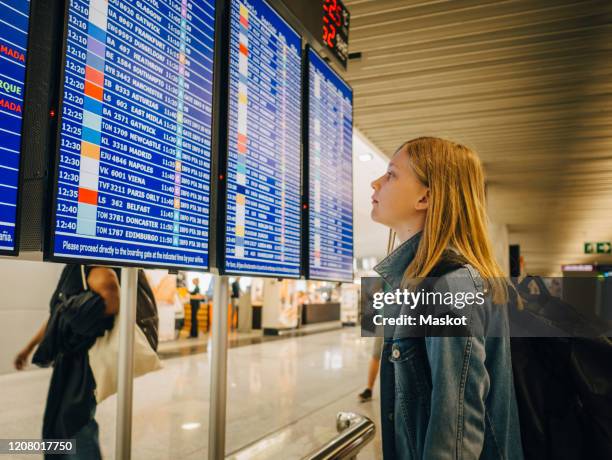 side view of girl looking at departure board while standing at airport - arrival time stock pictures, royalty-free photos & images