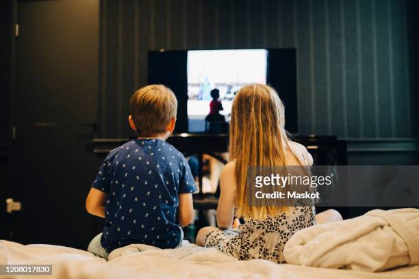 rear view of siblings watching television while sitting on bed in hotel room - family watching tv from behind stockfoto's en -beelden