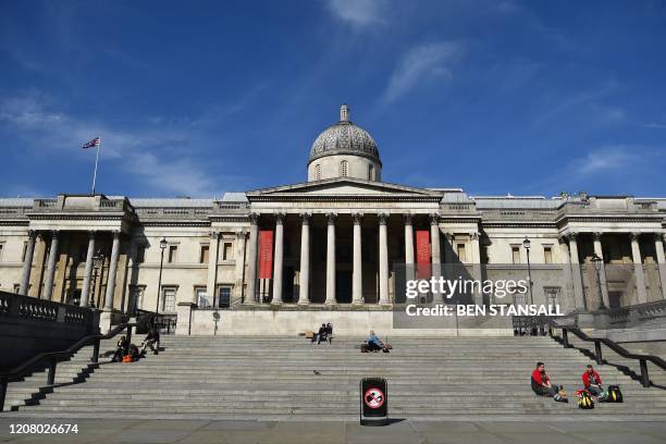 People sit on the steps outside the National Gallery in Trafalgar Square in the sunshine at lunch time, central London, March 23 as governments...
