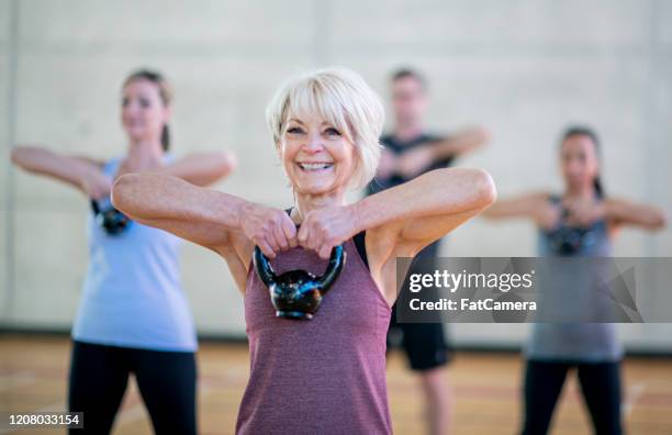 mujer senior en clase fitness usando una foto de stock de kettlebell - ejercicio fotografías e imágenes de stock