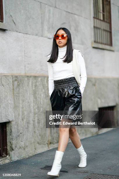 Yuwei Zhangzou wears sunglasses, a white turtleneck top, black leather shorts, white high heeled boots, outside Bottega Veneta, during Milan Fashion...