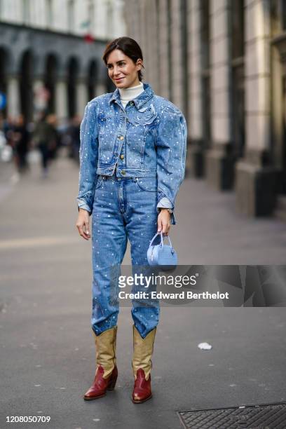 Gala Gonzalez wears a blue denim jacket with shoulder pads, a white turtleneck pullover, blue denim pants, cowboy boots, a bag, outside Philosophy,...