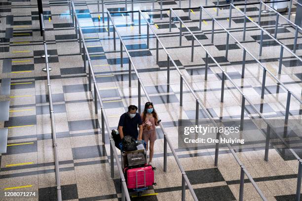 Travellers wearing face masks walk towards the taxi stand at the arrival hall of Changi Airport on March 23, 2020 in Singapore. Singapore is imposing...