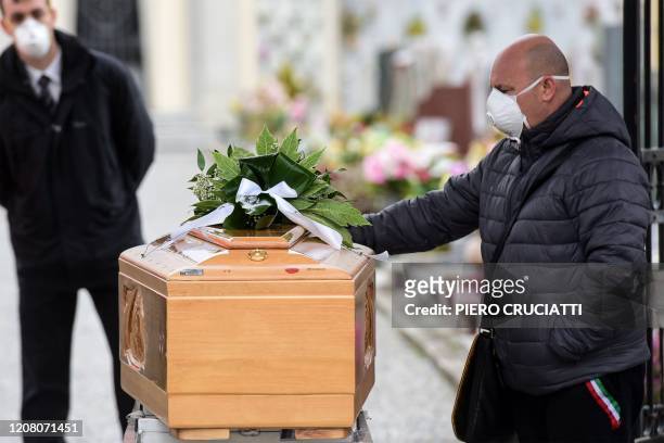 Man wearing a face mask touches the coffin of a deceased relative during a funeral ceremony at the entrance of the small cemetery of Bolgare,...