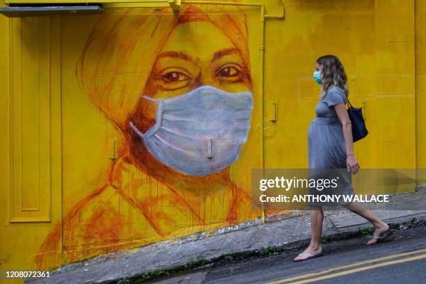 Pregnant woman wearing a face mask as a precautionary measure walks past a street mural in Hong Kong, on March 23 after the citys Chief Executive...