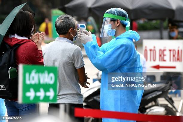 Health worker wearing a protective clothing amid concerns of the spread of the COVID-19 coronavirus, checks temperatures of visitors at the entrance...