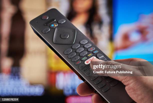 Detail of a mans hand pressing the Netflix button on a TV remote control, with Netflix streaming on a television in the background, taken on March 6,...