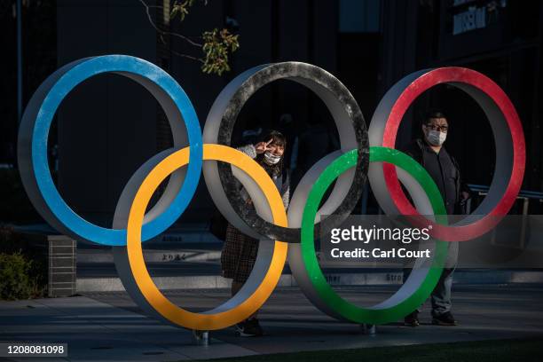 People wearing face masks pose for photographs next to Olympic Rings on March 24, 2020 in Tokyo, Japan. Although an official decision is yet to be...