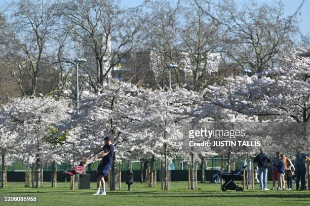 Man swings a little girl as they play in front of the blossom in Battersea Park in London on March 24, 2020 after Britain's government ordered a...
