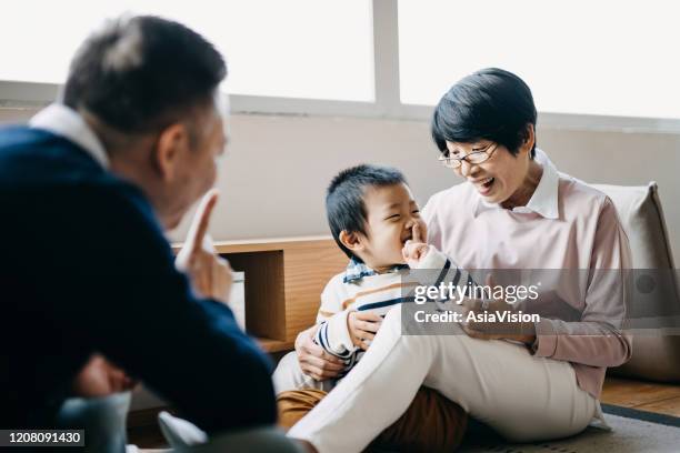 fröhliche asiatische großeltern, die im wohnzimmer auf dem boden sitzen und mit dem kleinen enkel plaudern und spielen - grandmas living room stock-fotos und bilder