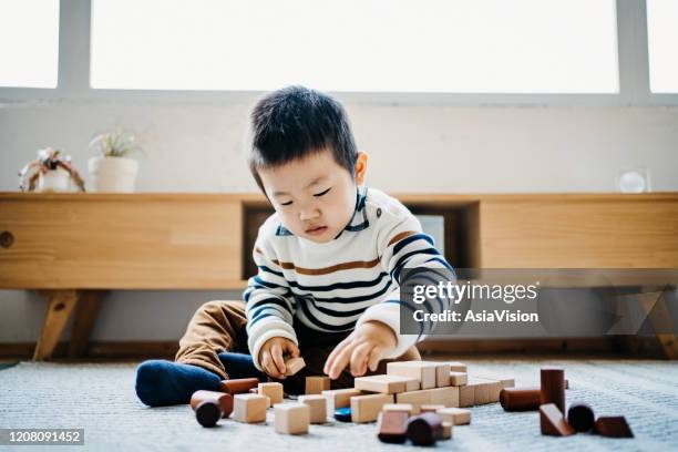 cute little boy sitting on the floor in the living room playing wooden building blocks - childrens play blocks stock pictures, royalty-free photos & images