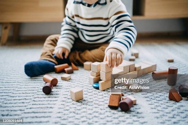 close up of cute little boy sitting on the floor in the living room playing wooden building blocks - wood block stacking stock pictures, royalty-free photos & images