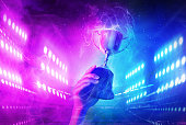 Trophy with smoke effect holding on hand and background blue and violet light for e-sport winner event.