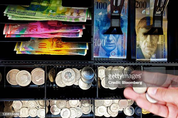 Teller handles Swiss franc coins at a till in this arranged photograph in Zurich, Switzerland, on Thursday, Aug. 11, 2011. The franc weakened after...