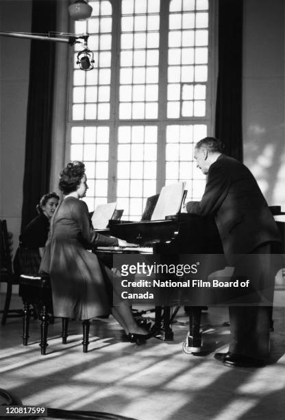 Henri Gagnon , Canadian composer, organist, and music educator, is standing next to a female student during a piano rehearsal at the Conservatoire de...