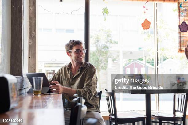 young man working on tablet computer in brightly lit cafe - regarder par dessus son épaule photos et images de collection