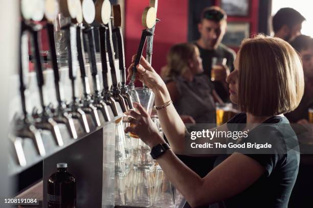 female bartender pouring beer at microbrewery - microbrewery stock pictures, royalty-free photos & images