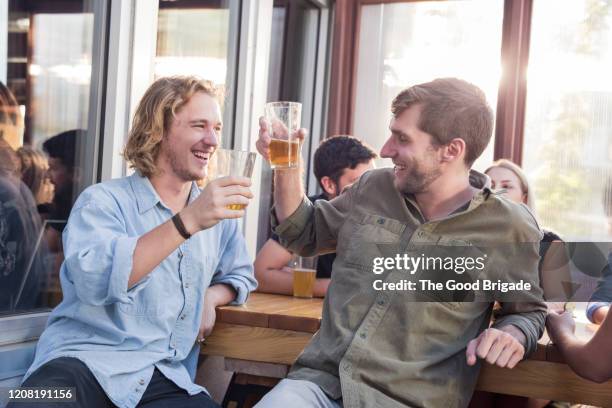 male friends toasting beer glasses at pub - man sipping beer smiling stockfoto's en -beelden