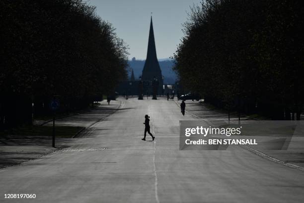 This picture taken on March 23, 2020 shows a runner crossing a road closed to traffic as she exercises in Greenwich Park in south London, as people...